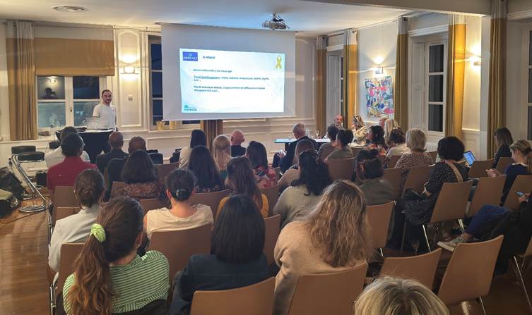 The image shows a presentation or seminar room with an audience of people, some seated, some standing, all facing a speaker at the front, who is using a slide presentation on a projector.
Le contenu généré par l’IA peut être incorrect.